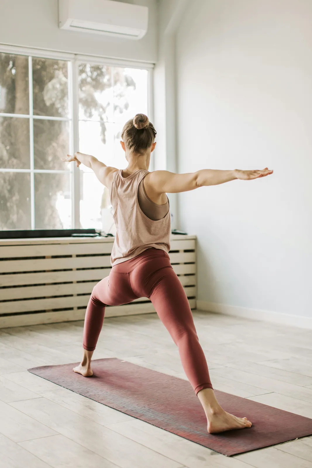 A woman holding warrior pose facing a studio window