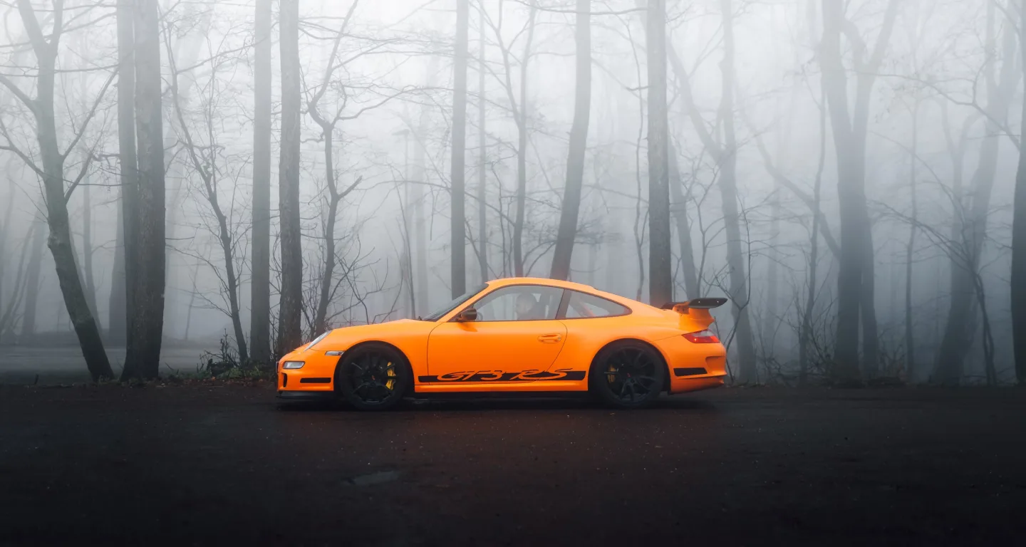 An orange sports car parked on a forest road