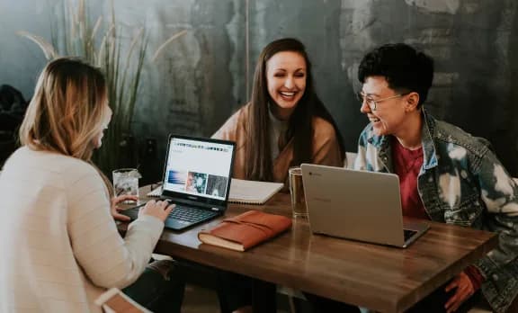 A team laughing around a table of laptops and notebooks