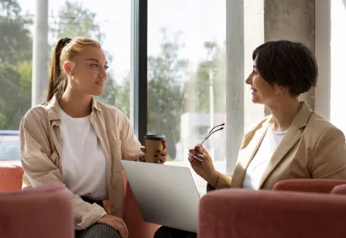 Two colleagues in armchairs comparing notes over a laptop